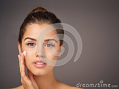 Nourished skin is beautiful skin. Studio portrait of a beautiful young woman applying moisturizer to her face against a Stock Photo