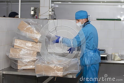 Meat factory. An enterprise worker in a protective suit and a medical mask is packing boxes Editorial Stock Photo