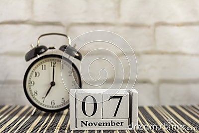 November 7 on a wooden calendar next to an alarm clock on a dark table .One day of the autumn month.Calendar for November. Autumn Stock Photo