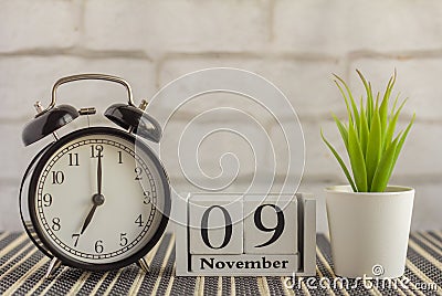 November 9 on a wooden calendar next to an alarm clock on a dark table .One day of the autumn month.Calendar for November. Autumn Stock Photo