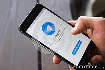 Novosibirsk, Russia - April 30, 2018 - Male hand holding smartphone with the start window of the Telegram application. Wooden back Editorial Stock Photo