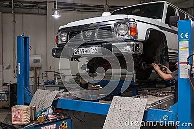 White used car Nissan Patrol raised on a blue lift for repairing the chassis and engine in a vehicle repair shop. Auto service Editorial Stock Photo