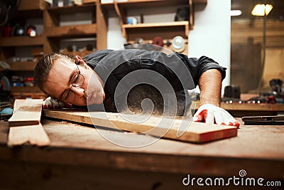 Now for the finishing touch. a focused young male carpenter blowing dust off of a piece of wood after sanding it inside Stock Photo