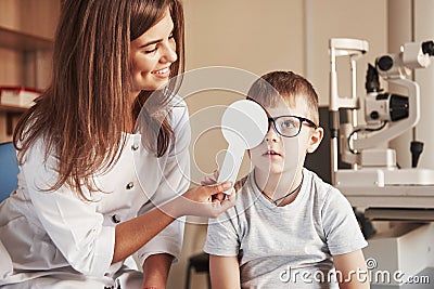 Now tell me what you see. Female doctor covers kid eye with medical tool for checking visual acuity Stock Photo