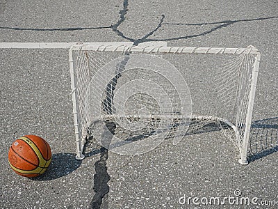 Noyabrsk, Russia - August 9, 2020: An orange-and-yellow basketball with a shadow next to a small soccer goal on the concrete floor Editorial Stock Photo