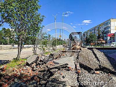 Noyabrsk, Russia - July 6, 2022: The bulldozer removes the old roadbed from the sidewalk. Broken pieces of asphalt and bricks are Editorial Stock Photo