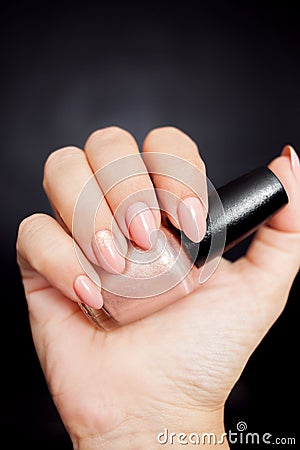 Nude manicure with gold decor. Womens hand holding a bottle of nail Polish Stock Photo