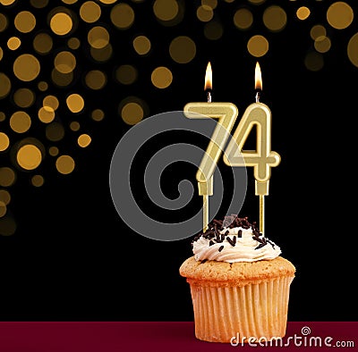 Number 74 birthday candle - Cupcake on black background with out of focus lights Stock Photo