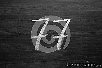 Number seventy seven enumeration written with a chalk on the blackboard Stock Photo