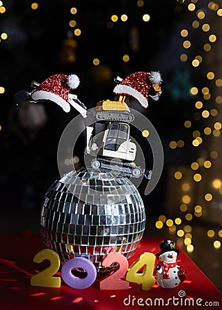 numbers 2024, models of toy excavators stand on a mirrored disco ball, bokeh from garlands Stock Photo