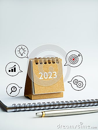 2023 numbers year on small beige desk calendar cover on notepad with pen and business process and success icons. Stock Photo