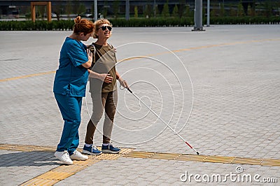 A nurse accompanies an elderly blind woman on a walk. Stock Photo