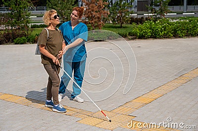 A nurse accompanies an elderly blind woman on a walk. Stock Photo