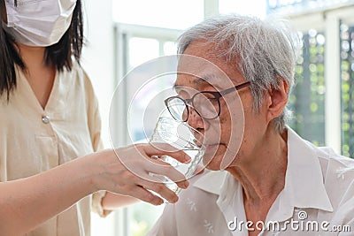 Nurse or caregiver gives water to senior woman,taking care,feeding water,thirsty asian old elderly drinking fresh water to quench Stock Photo