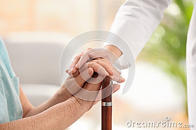 Nurse comforting elderly woman with cane against blurred background. Assisting senior generation Stock Photo