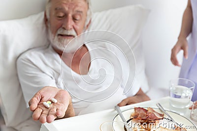 Nurse give medicine pills to elderly senior patient while he is in his bed with breakfast Stock Photo