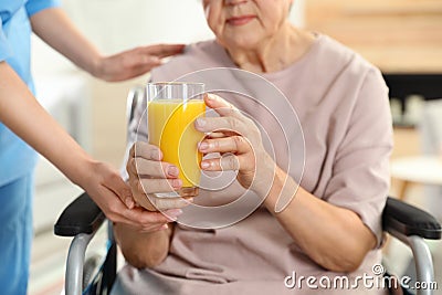 Nurse giving glass of juice to elderly woman indoors. Assisting senior people Stock Photo