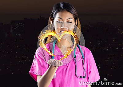 nurse with hand spread of with heart fire icon over in front of the city at night. Stock Photo