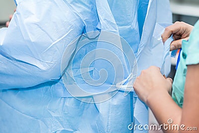 Nurse helping doctor getting dressed with disposable sterile clothes for surgery Stock Photo