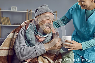 Nurse taking care of a sick retired senior man, helping him and making him hot tea Stock Photo