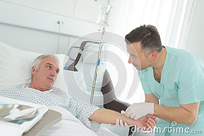 Nurse inserting needle into arm senior male hospital patient Stock Photo