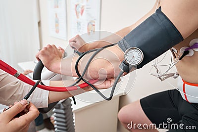 The nurse measures arterial tension. Man patient, pedaling on a bicycle ergometer stress test system for the function of Stock Photo