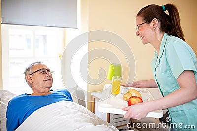 Nurse in a old peopleâ€™s home providing residential care by bringing breakfast to her senior man occupant Stock Photo