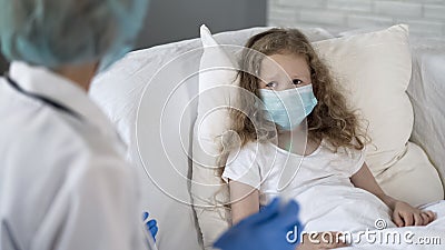 Nurse preparing to make injection to scared girl, wearing face mask, infection Stock Photo