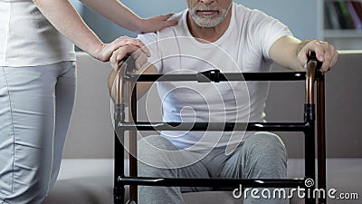 Nurse supporting male pensioner holding walking frame, rehabilitation center Stock Photo