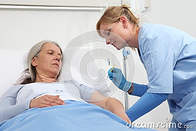 Nurse with the syringe injects the vaccine to the elderly woman patient lying in the hospital room bed Stock Photo