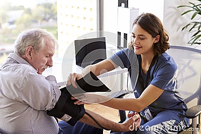 Nurse Wearing Scrubs In Office Checking Senior Male Patients Blood Pressure Stock Photo