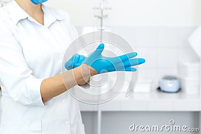 A nurse in a white coat puts on rubber gloves before a medical procedure in a bright handling room Stock Photo