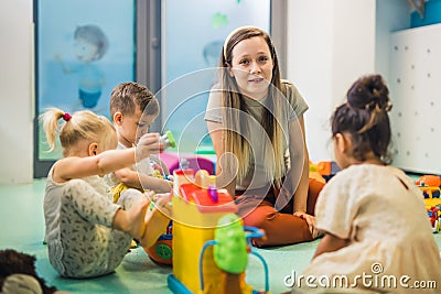 Nursery school. Toddlers and their teacher playing with colorful plastic playhouses, cars and boats. Imagination Stock Photo