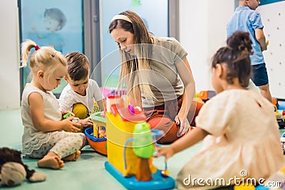 Nursery school. Toddlers and their teacher playing with colorful plastic playhouses, cars and boats. Imagination Stock Photo