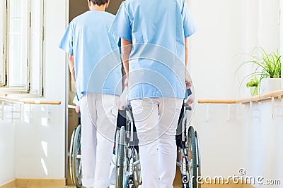 Nurses pushing seniors in wheelchair thru nursing home Stock Photo