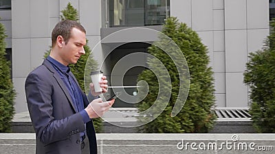 O homem de neg?cios novo que anda abaixo da rua com um vidro do caf? em sua m?o escreve uma mensagem no telefone vídeos de arquivo O homem de neg?cios novo que anda abaixo da rua com um vidro do caf? em sua m?o escreve uma mensagem no telefone vídeos de arquivo