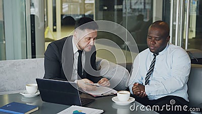 O homem de negócios irritado no terno de negócio preto critica severamente seu empregado afro-americano durante a reunião no café video estoque O homem de negócios irritado no terno de negócio preto critica severamente seu empregado afro-americano durante a reunião no café video estoque