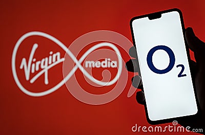 O2 Telefonica logo on smartphone screen hold in hand and Virgin Media logo on blurred background. Concept for Virgin and O2 merger Editorial Stock Photo