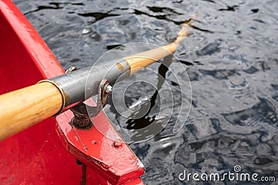 Oar is held on an oarlock attached to a red boat, against the background of water. Stock Photo