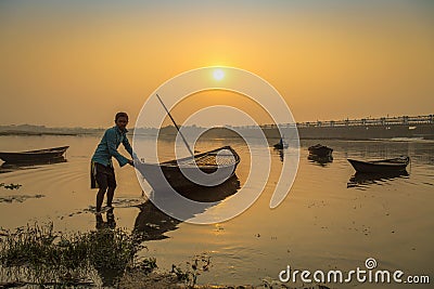 An oarsman tries to tow his boat to shore at sunset on river Damodar. Editorial Stock Photo