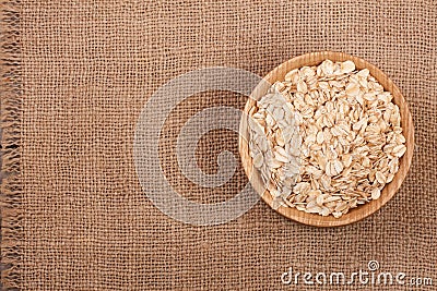 Oat flakes in a wooden bowl on sackcloth with copy space for your text. Top view Stock Photo