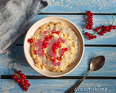 Oatmeal for breakfast with red currants on a blue wooden tray, spoon and denim napkin Stock Photo