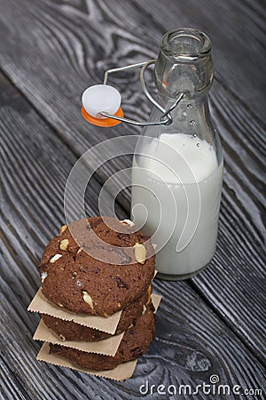 Oatmeal cookies with peanuts and chocolate. Folded in a column and laid out with paper. Nearby milk. On pine boards Stock Photo