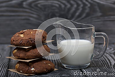 Oatmeal cookies with peanuts and chocolate. Folded in a column and laid out with paper. Nearby milk. On pine boards Stock Photo