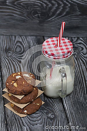 Oatmeal cookies with peanuts and chocolate. Folded in a column and laid out with paper. Nearby milk. On pine boards Stock Photo