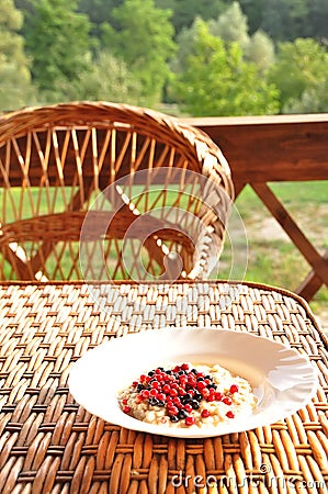 Oatmeal with forest different berries on the terrace table with a beautiful view of nature. Stock Photo