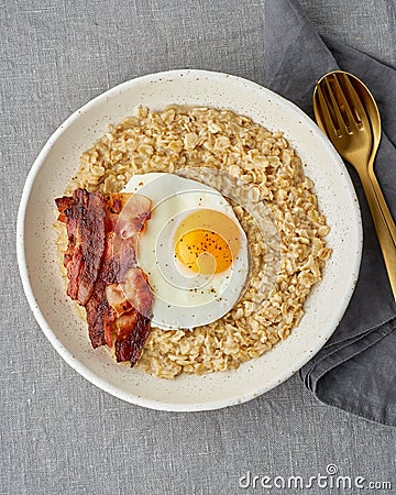 Oatmeal, fried egg and fried bacon. Hearty fat high-calorie breakfast, source of energy. Vertical Stock Photo