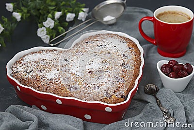 Oatmeal pie with cherry dusted with powdered sugar in a ceramic form in the shape of a heart on a dark background Stock Photo
