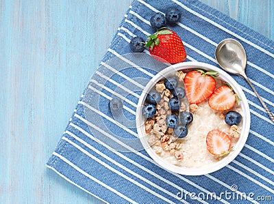 Oatmeal porridge with fresh strawberry, blueberry, granola on contrast blue background. Healthy breakfast. Top view. Stock Photo