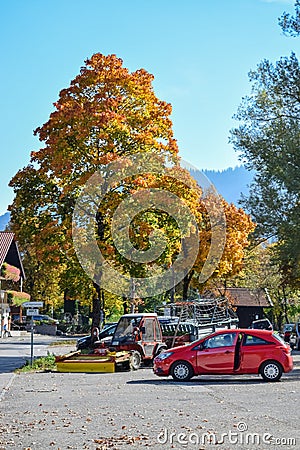OBERAMMERGAU, GERMANY - OKTOBER 09, 2018: Car and tractor under a yellow tree in the autumn afternoon in Alps Editorial Stock Photo